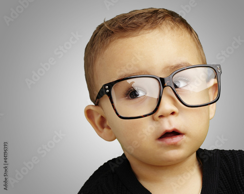 Photo: portrait of kid wearing glasses over grey background portrait of kid wearing glasses over grey background