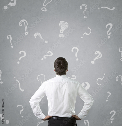 Photo: Young businessman looking at many question marks Young businessman looking at many question marks