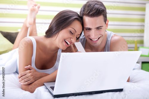 Photo: Couple in bed buying on-line with credit card Couple in bed buying on-line with credit card