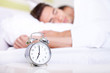Young couple lying in white bed with alarm clock