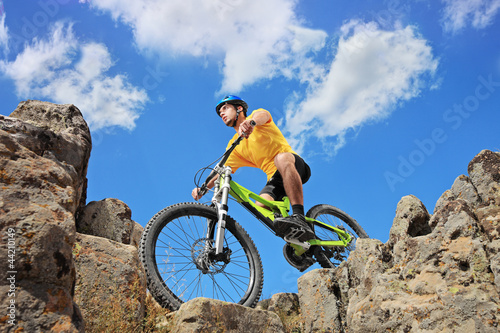 Photo: Person riding a mountain bike amid rocks on a sunny day against Person riding a mountain bike amid rocks on a sunny day against