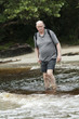 senior man is crossing a river with his backpack