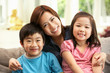 Chinese Mother And Children Sitting On Sofa At Home Together