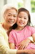 Chinese Grandmother And Granddaughter Relaxing On Sofa At Home