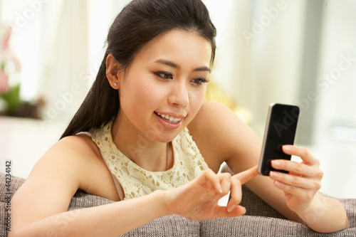 Photo: Young Chinese Woman Using Mobile Phone On Sofa At Home Young Chinese Woman Using Mobile Phone On Sofa At Home