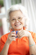 Senior Chinese Woman Drinking Tea On Sofa At Home