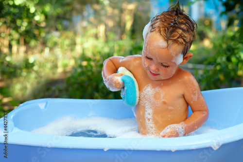 Photo: baby boy washes with sponge in bubble bath outdoor baby boy washes with sponge in bubble bath outdoor