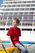 little boy sitting in front of ship in port