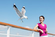 Smiling woman  feeds seagulls with bread on deck of ship.