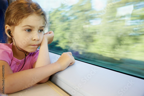 Foto: Girl listens to music, sitting by window of moving speed train Girl listens to music, sitting by window of moving speed train
