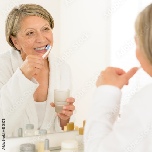 Photo: Senior woman brushing teeth bathroom mirror reflection Senior woman brushing teeth bathroom mirror reflection