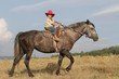 young happy boy in cowboy hat riding horse on natural background