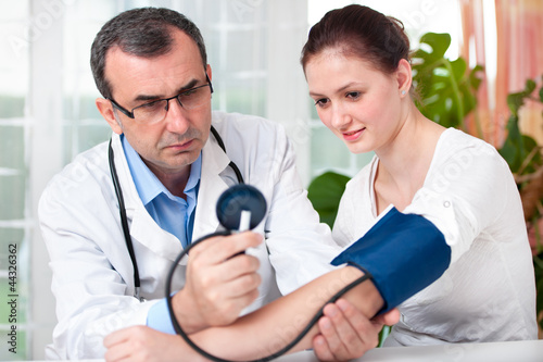 Photo: Arzt misst den Blutdruck und Puls bei Patientin Arzt misst den Blutdruck und Puls bei Patientin