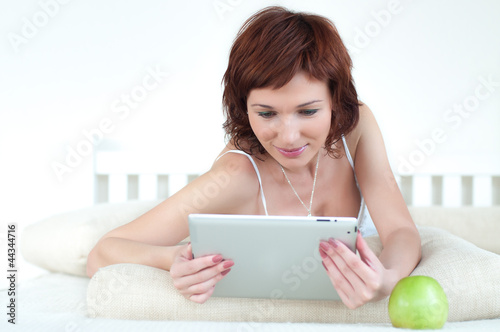 Photo: woman with an green apple and tablet at bed reading ebook woman with an green apple and tablet at bed reading ebook