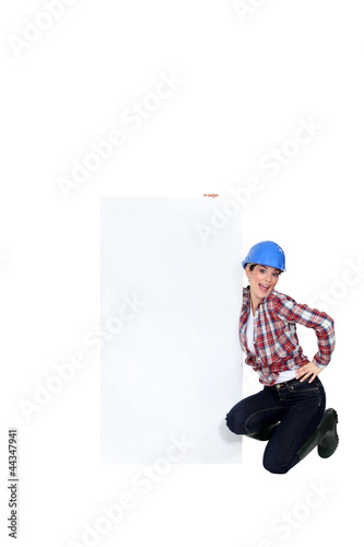 Photo: Female builder kneeling by blank poster Female builder kneeling by blank poster