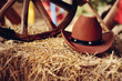 on a haystack the brown cowboy's hat and a wooden wheel lies
