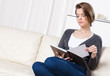 Young girl reads the book sitting on the white leather sofa