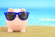 Foto: Summer piggy bank with sunglasses on the beach Summer piggy bank with sunglasses on the beach
