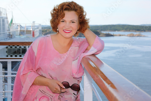 Photo: Happy woman stands at ship deck at background of beautiful coast Happy woman stands at ship deck at background of beautiful coast