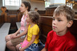 Mother, daughter and son sit on bench in Catholic Church