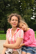 Happy mother and daughter sit in park. Little girl hugs mother