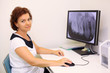 Dentist sits at table with big jaw x-ray image on monitor