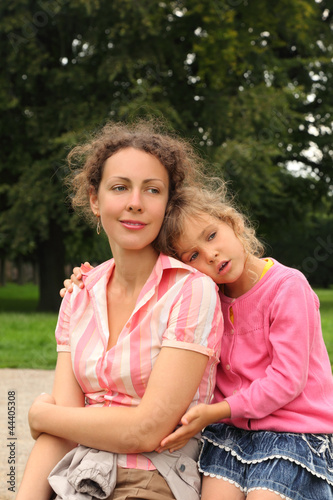 Photo: Happy mother and daughter sit in park. Little girl hugs mother Happy mother and daughter sit in park. Little girl hugs mother