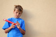 Boy with big red pencil stands near wall and closes pencil