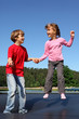 Happy brother and sister jump on trampoline on sunny summer day