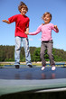 Joyful brother and sister jump on trampoline at sunny summer day