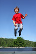 Joyful boy dressed in red T-shirt jumps on trampoline