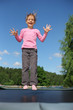 Joyful girl dressed in pink T-shirt jumps on trampoline
