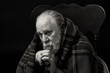 Old man wrapped in shawl sits quietly thinking