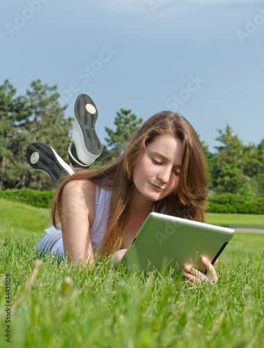 Photo: Young girl using a tablet in the park Young girl using a tablet in the park