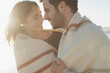 Smiling couple wrapped in blanket and hugging on beach