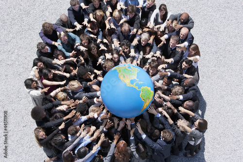 Photo: Crowd of business people in huddle reaching for globe Crowd of business people in huddle reaching for globe