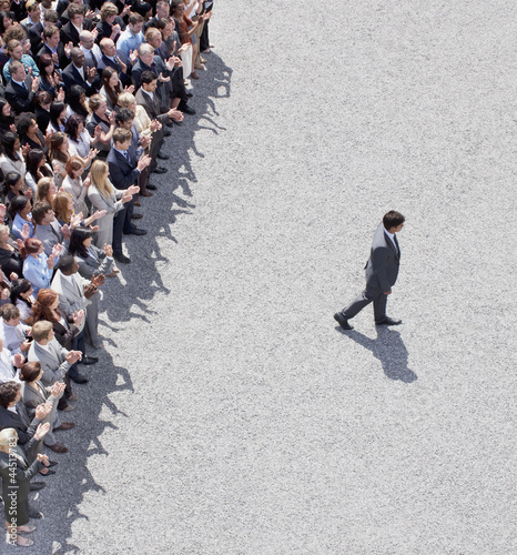 Photo: Businessman walking away from clapping crowd Businessman walking away from clapping crowd