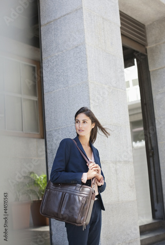 Photo: Businesswoman with briefcase in front of urban building Businesswoman with briefcase in front of urban building