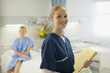 Portrait of smiling nurse holding medical record in hospital room
