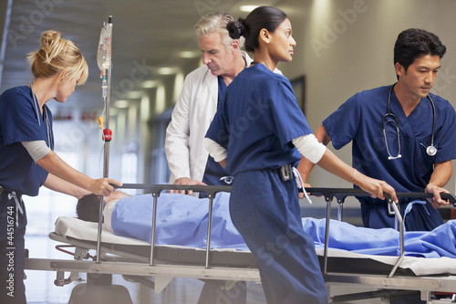 Photo: Doctor and nurses wheeling patient in gurney through hospital corridor Doctor and nurses wheeling patient in gurney through hospital corridor