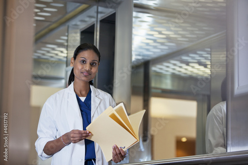 Photo: Portrait of confident doctor holding medical record in hospital elevator Portrait of confident doctor holding medical record in hospital elevator