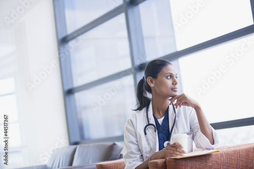Photo: Pensive doctor drinking coffee and looking out window Pensive doctor drinking coffee and looking out window