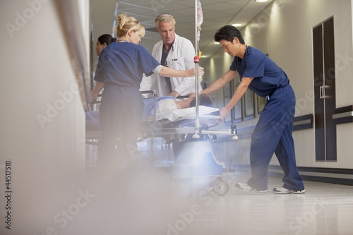 Photo: Doctors and nurses wheeling patient on gurney in hospital corridor Doctors and nurses wheeling patient on gurney in hospital corridor