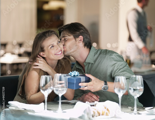 Photo: Man kissing and giving gift to woman in restaurant Man kissing and giving gift to woman in restaurant