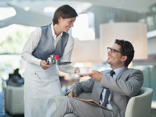 Photo: Waitress serving businessman cup of coffee in hotel lounge Waitress serving businessman cup of coffee in hotel lounge
