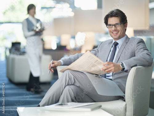 Photo: Portrait of smiling businessman reading newspaper in lounge Portrait of smiling businessman reading newspaper in lounge