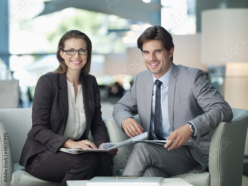 Photo: Portrait of smiling businessman and businesswoman working in lobby Portrait of smiling businessman and businesswoman working in lobby