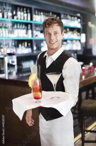 Photo: Portrait of smiling bartender holding tray with cocktails in bar Portrait of smiling bartender holding tray with cocktails in bar