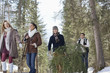 Friends carrying fresh cut Christmas tree in woods