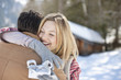 Smiling woman holding Christmas gift and hugging man in snowy field